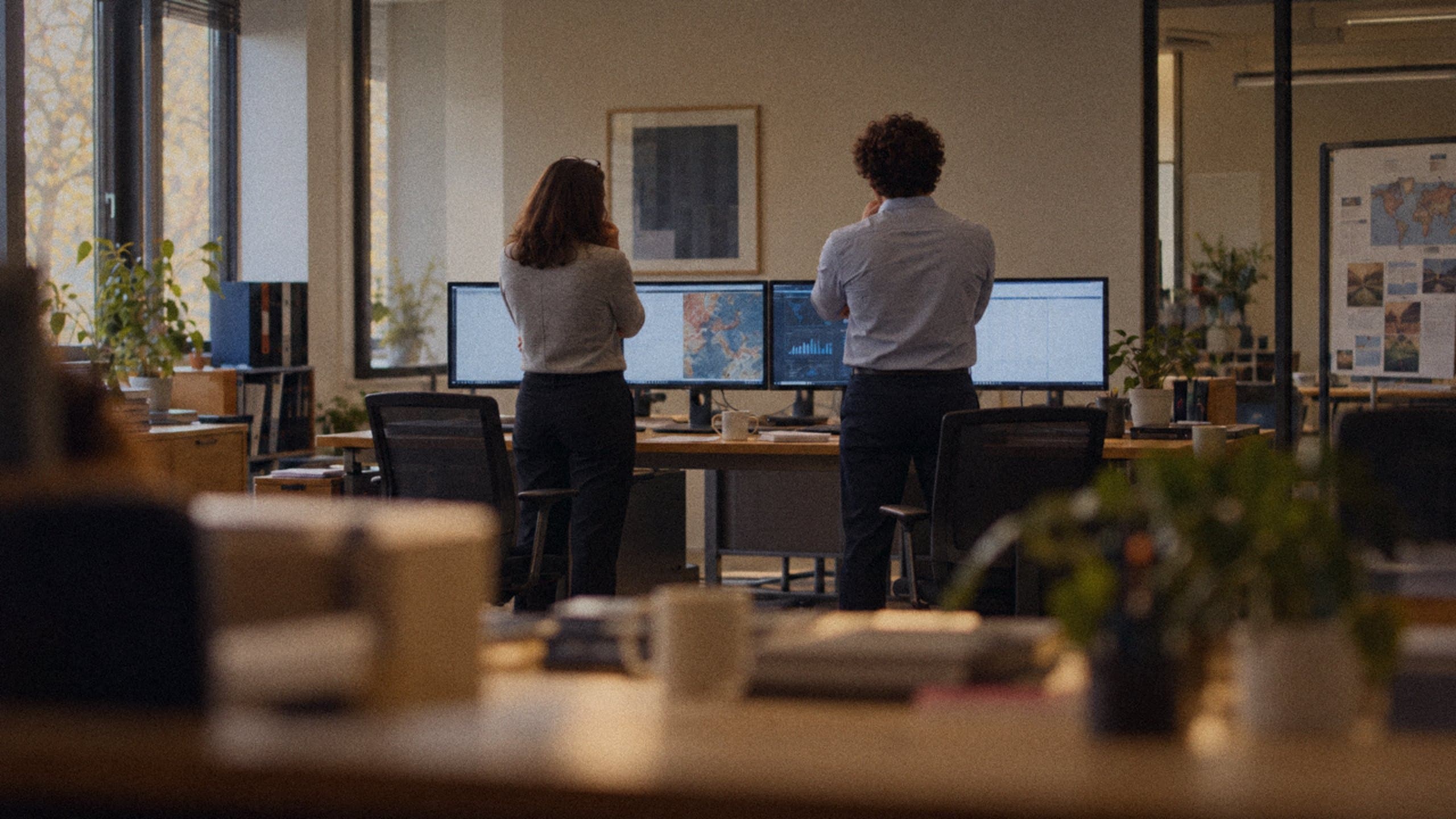 An engineer and an employee standing at the desk, watching the screens together.