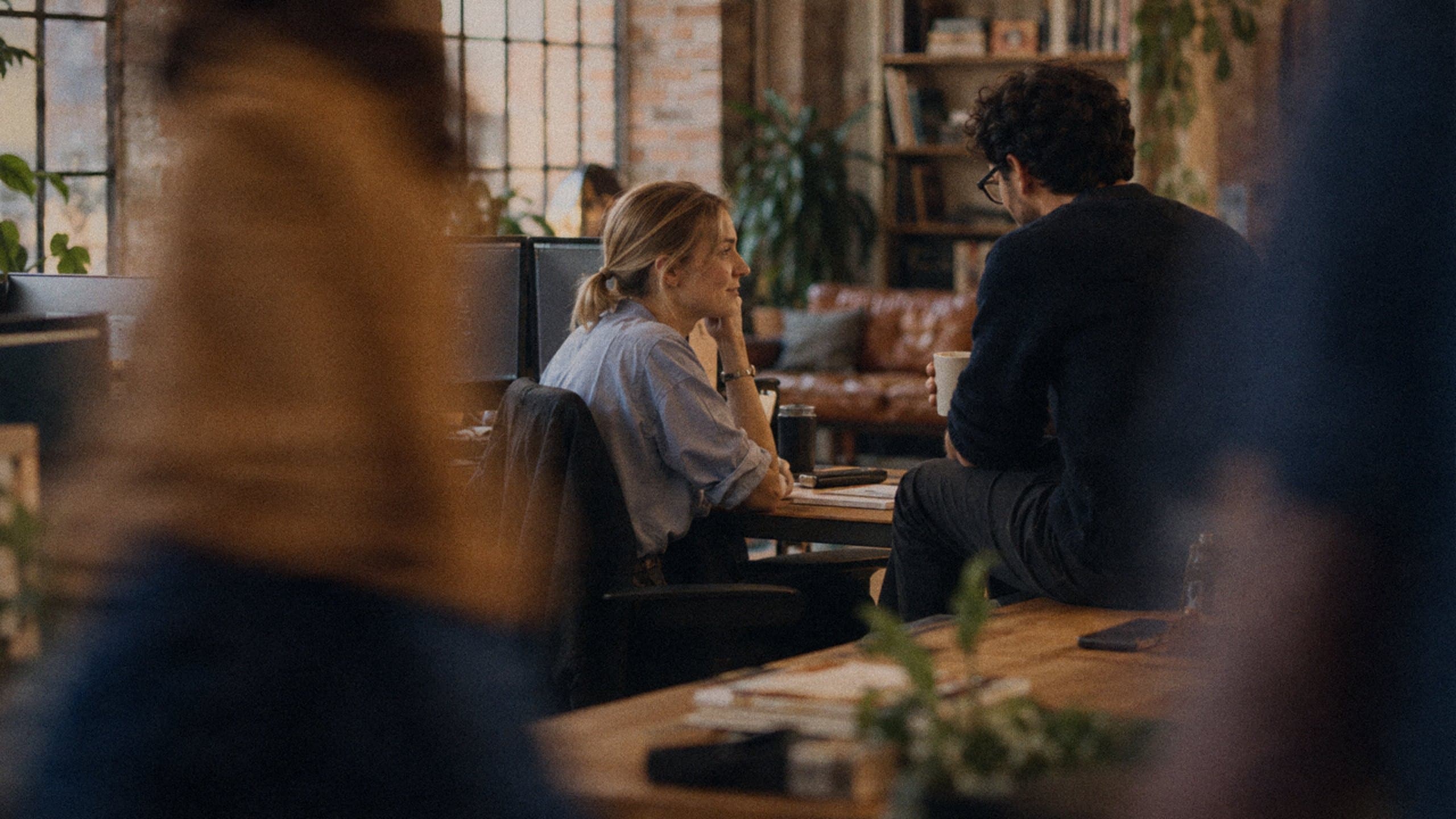 Two engineers talking over coffee at a desk in a warm loft office.